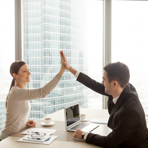 Businessman giving high five to businesswoman at office, partners celebrating good successful teamwork result, business team happy with job well-done, business achievement, company growth, side view
